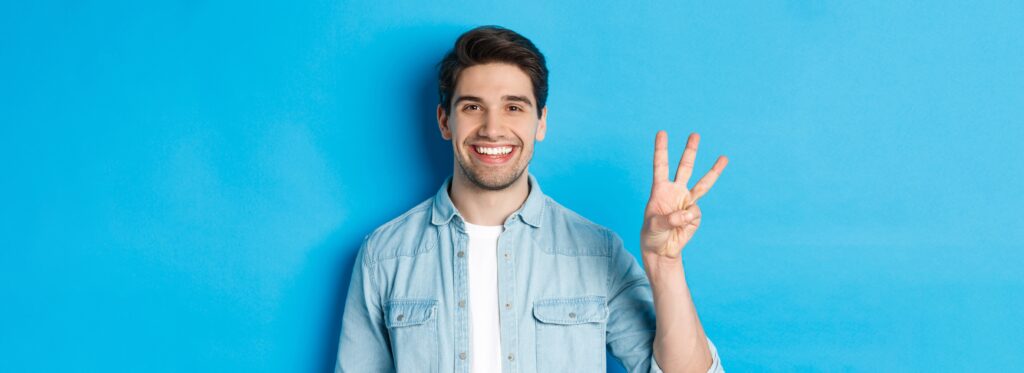 Homem de cabelo curto e camisa jeans clara fazendo o sinal de três com a mão